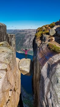 A lone hiker stands on the edge of the Kjeragbolten, Norway cliff in Norway, enjoying the stunning view of the fjord below. Asian women visit Kjeragbolten, Norway