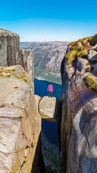 A lone hiker stands on the edge of Kjeragbolten, a cliff in Norway, looking out over the vast Norwegian landscape.