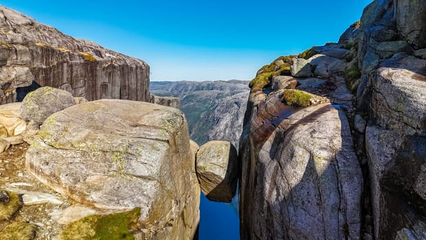 A scenic view of Kjeragbolten, Norway, a dramatic rock formation in Norway, where a large boulder appears to be precariously balanced between two cliffs.