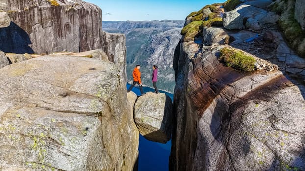 Two hikers stand on a rock formation at the edge of Kjeragbolten, Norway, looking out over the vast expanse below. a couple visiting Kjeragbolten Norway