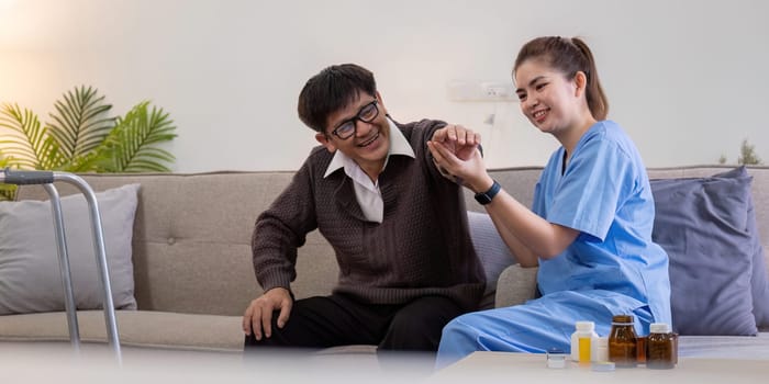 A caregiver in blue scrubs helps an elderly man with physical therapy exercises at home, promoting health and well-being.