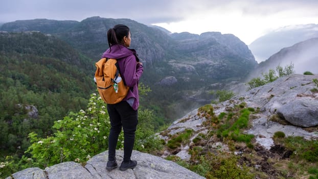 A lone hiker stands on a rocky outcrop, gazing out over a stunning Norwegian fjord landscape. The mist hangs low in the valleys, adding an ethereal quality to the scene. Preikestolen, Norway