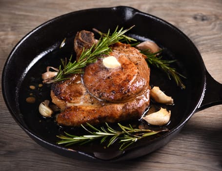 Pork cutlet on the bone in a piece of butter with garlic and rosemary in a frying pan 