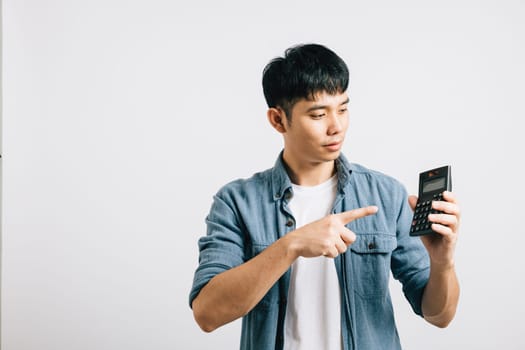 A young man, isolated on grey, points at a calculator number, conveying the success of tax calculation. His smile reflects financial achievement and career progress.