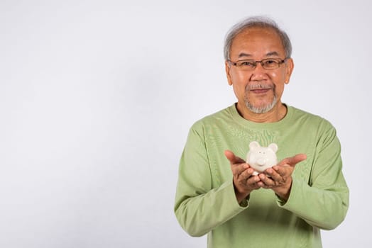 Portrait smiling Asian older man holding white piggy bank on hand studio shot isolated on white background, Concept of responsibility and financial planning, Saving money after retirement