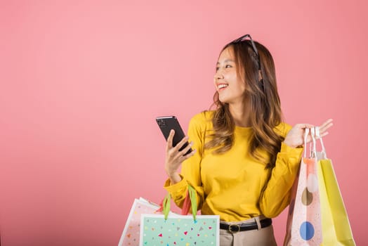 Portrait Asian happy beautiful young woman teen shopper smiling standing excited holding online shopping bags online colorful on mobile phone or smartphone studio shot isolated on pink background