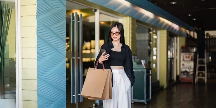 A fashionable woman holding brown paper shopping bags while checking her phone in a contemporary shopping mall during Black Friday.