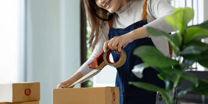 Young business entrepreneur sealing a box with tape. Preparing for shipping, Packing, online selling, e-commerce concept.