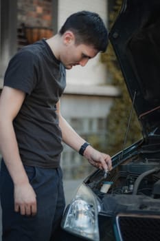 One young Caucasian guy holding in his hand a burnt-out lamp from the right front headlight of a car, standing half-turn on a city street on a summer day in the evening, close-up side view. Concept for replacing light bulbs, car repair.