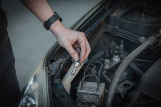 One young Caucasian unrecognizable guy holds in his hand a burnt-out lamp from the right front headlight of a car, standing on a city street on a summer day in the evening, close-up top view. Concept for replacing light bulbs, car repair.