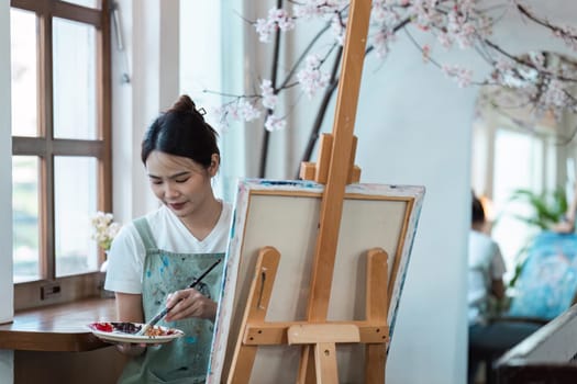 A young woman painting on a canvas in her home studio, surrounded by natural light and a blossoming cherry tree, highlighting the joy and tranquility of engaging in a creative hobby.