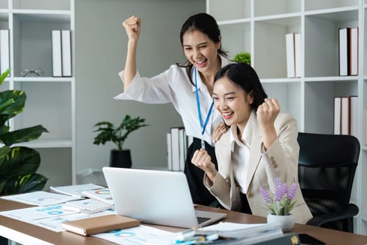 Two women are celebrating in a cubicle with a laptop on the desk. Scene is happy and positive
