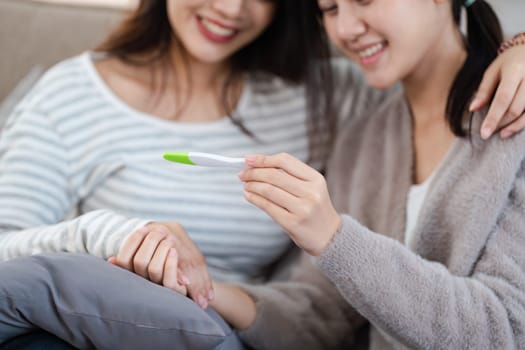 Two happy gay lesbian lgbt women couple sitting on sofa celebrating positive pregnancy test. lgbtq concept .