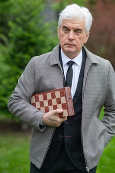 Elderly Caucasian man holding chess outdoors. Vertical photo