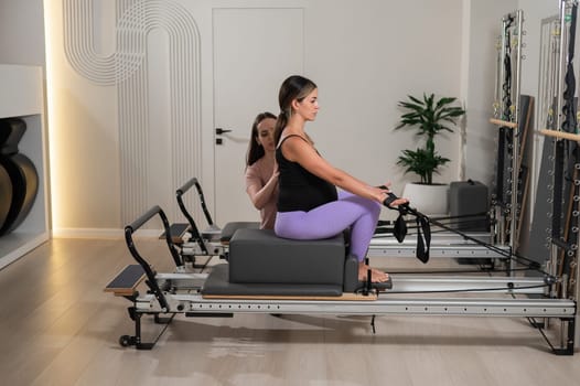 Caucasian pregnant woman doing Pilates exercises on a reformer machine with an individual trainer