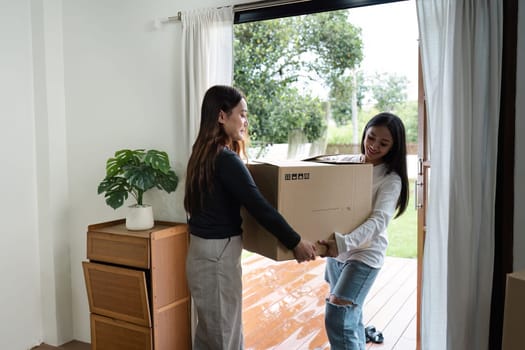 Lesbian couple moving into their new home, carrying a box together, smiling and enjoying the moment. LGBT love and lifestyle, modern home interior.
