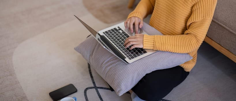 A person in a cozy home environment working on a laptop, sitting on the floor with a pillow for support, showcasing a comfortable and modern lifestyle at home.