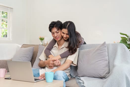 Young couple embracing on a couch, using a laptop, in a cozy living room setting. Ideal for lifestyle, home comfort, and relationship themes.