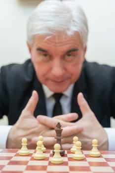 Elderly Caucasian man looking at camera while playing chess. Vertical photo