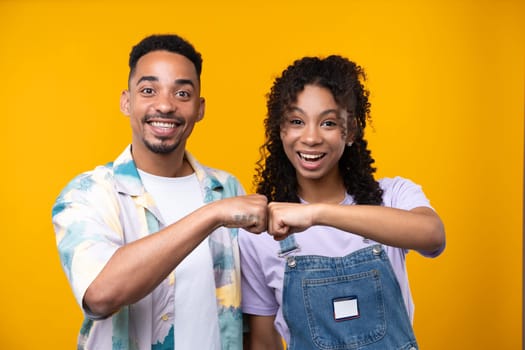 Two hipster friends smiling cheerfully while standing against a yellow background. High quality photo