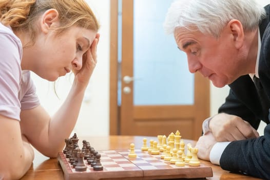 An elderly man and a middle-aged woman play chess