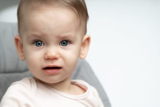 Baby makes a funny angry and sad face sitting in a chair