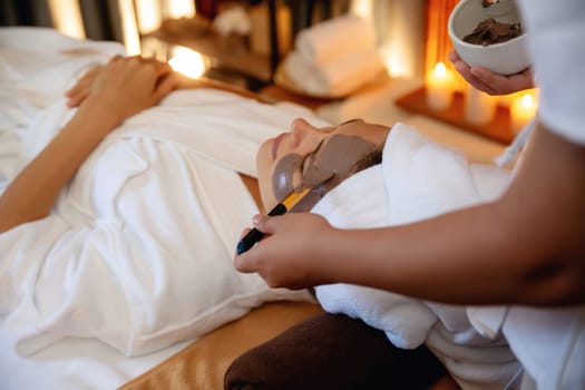 Serene ambiance of spa salon, woman customer indulges in rejuvenating with charcoal face cream massage with warm lighting candle. Facial skin treatment and beauty care concept. Quiescent