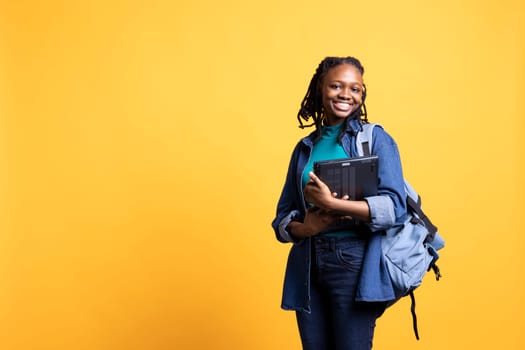 Portrait of cheerful woman carrying laptop needed to do school homework, isolated over studio background. Joyful pupil holding notebook, preparing for university assessment