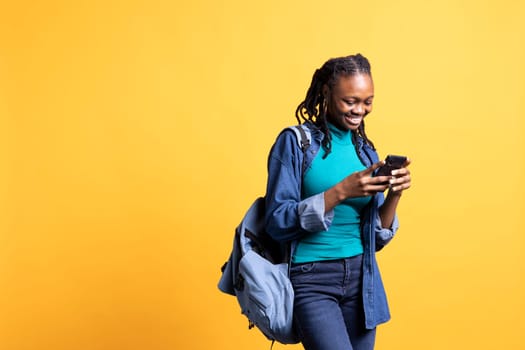 BIPOC woman texting best friend using smartphone, reading messages. Relaxed african american person having fun while chatting with mate on mobile phone, isolated over studio background