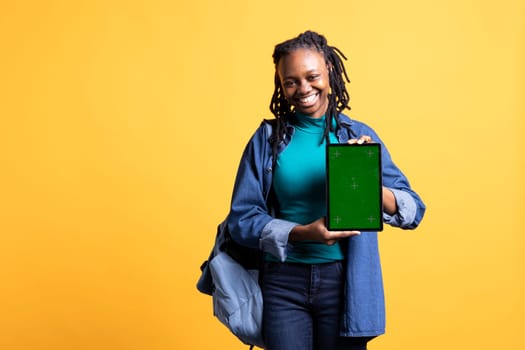 Smiling african american woman presenting tablet with green screen display, isolated over studio background. Cheerful BIPOC person creating promotion with blank copy space mockup device