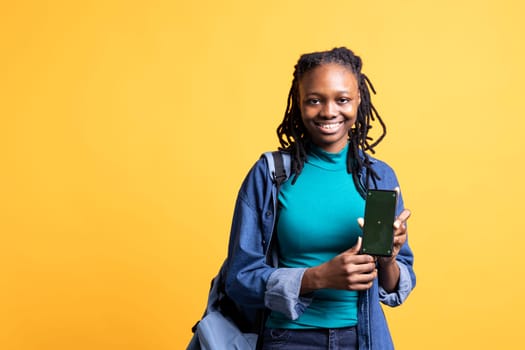 Jolly african american woman presenting smartphone with green screen display, isolated over studio background. Joyous BIPOC person creating promotion with blank copy space mockup phone