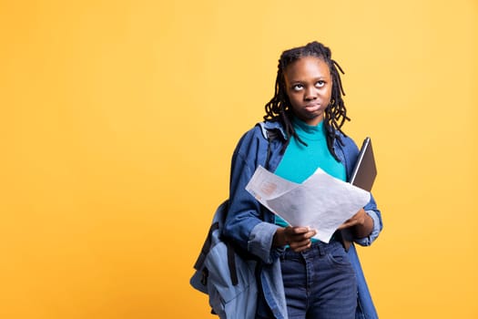 African american woman rolling eyes, working accounting job, looking at report pages, feeling bored, studio background. Young girl frustrated after reading paperwork all day while solving tasks