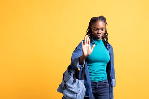 Assertive african american woman doing stop hand gesture. Annoyed BIPOC person doing firm halt sign gesturing, wishing to end concept, isolated over yellow studio background