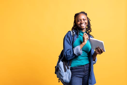 Portrait of cheerful young girl smiling, reading and writing for school exam on notepad, studio background. Joyous student holding exercise notebook with research done for university courses