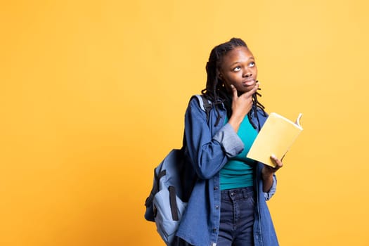 Portrait of BIPOC woman daydreaming while holding book, thinking of characters. Person with novel in arms caught in imagination while enjoying leisure time, isolated over studio background