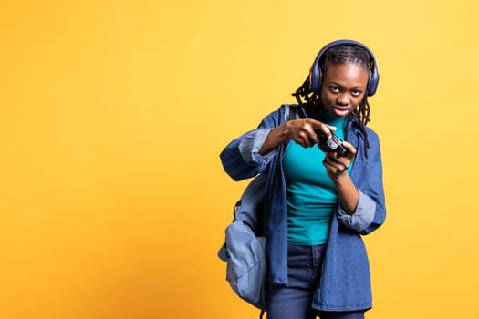 Portrait of young girl playing videogames with controller, hearing sounds through headphones, isolated over studio background. BIPOC gamer having fun participating in PvP internet game with joypad