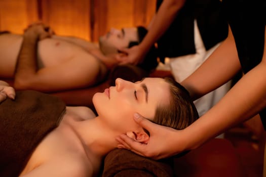 Couple customer enjoying relaxing anti-stress head massage and pampering facial beauty skin recreation leisure in warm candle lighting ambient salon spa in luxury resort or hotel. Quiescent