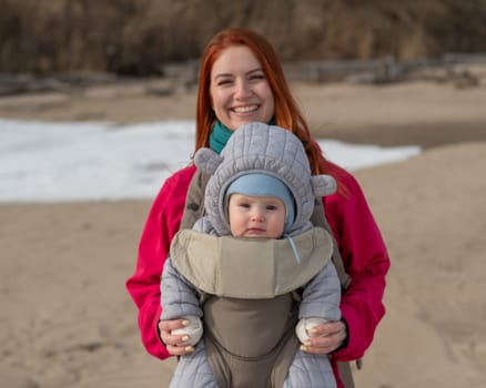 Caucasian red-haired woman walks with her son in an ergo backpack in nature in winter