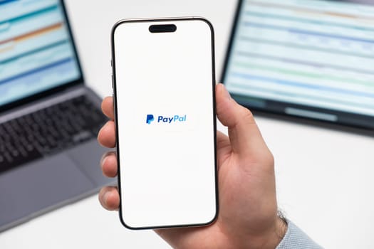 PRAGUE, CZECH REPUBLIC - JANUARY 21 2024: PayPal logo on the screen of smartphone in mans hand on the workplace background.