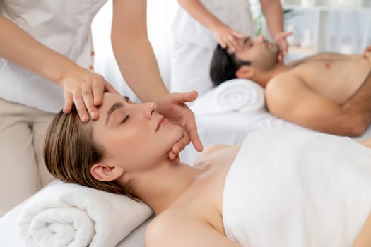 Caucasian couple enjoying relaxing anti-stress head massage and pampering facial beauty skin recreation leisure in dayspa modern light ambient at luxury resort or hotel spa salon. Quiescent