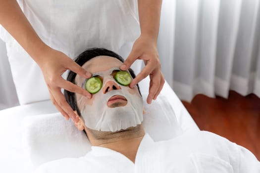 Serene daylight ambiance of spa salon, man customer indulges in rejuvenating with luxurious cucumber facial mask. Facial skincare treatment and beauty care concept. Quiescent