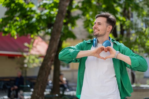 I love you. Caucasian man makes symbol of love, showing heart sign to camera, express romantic feelings, express sincere positive feelings. Charity, gratitude, donation. Outdoors in urban city street