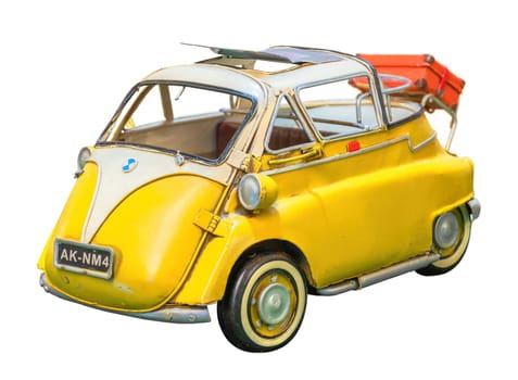 Isolated vintage yellow stand-alone toy replica of a retro car resembling a BMW Isetta clipped on a white background and featuring a sunroof with a luggage in the back evoking leisures and vacations.