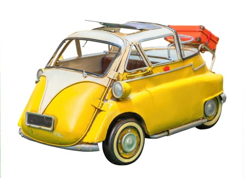Isolated vintage yellow stand-alone toy replica of a retro microcar clipped on a white background and featuring a sunroof with a luggage in the back evoking leisures and vacations.