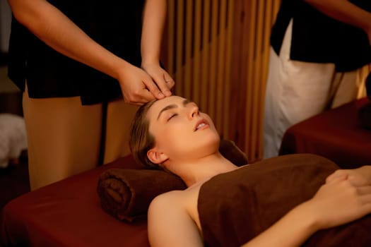 Caucasian woman enjoying relaxing anti-stress head massage and pampering facial beauty skin recreation leisure in warm candle lighting ambient salon spa in luxury resort or hotel. Quiescent