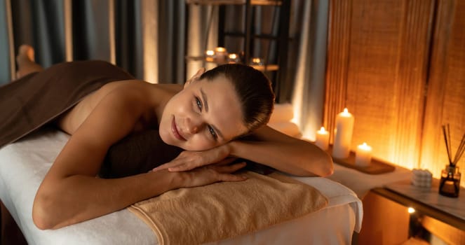 Caucasian woman customer enjoying relaxing anti-stress spa massage and pampering with beauty skin recreation leisure in warm candle lighting ambient salon spa at luxury resort or hotel. Quiescent