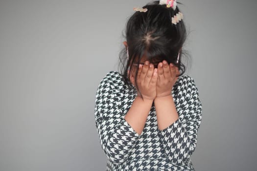 a upset child girl cover her face with hand .