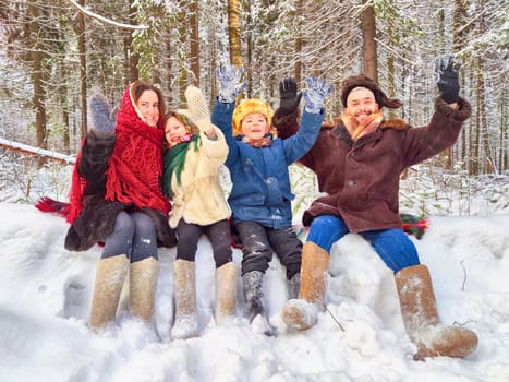 Joyful family ethnic dress with shawls and earflap hats in winter forest in carnival Maslenitsa in Russia. Tourists in Shrovetide in spring. Mother, father, son, daughter having fun in the snow