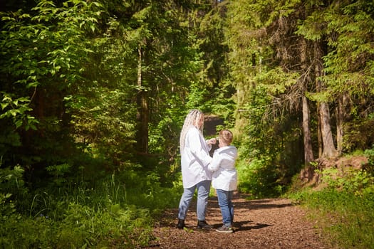 Funny mother with dreadlocks and fat boy happy walking in the forest on a sunny summer day