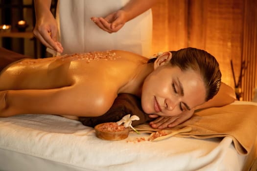 Woman customer having exfoliation treatment in luxury spa salon with warmth candle light ambient. Salt scrub beauty treatment in Health spa body scrub. Quiescent